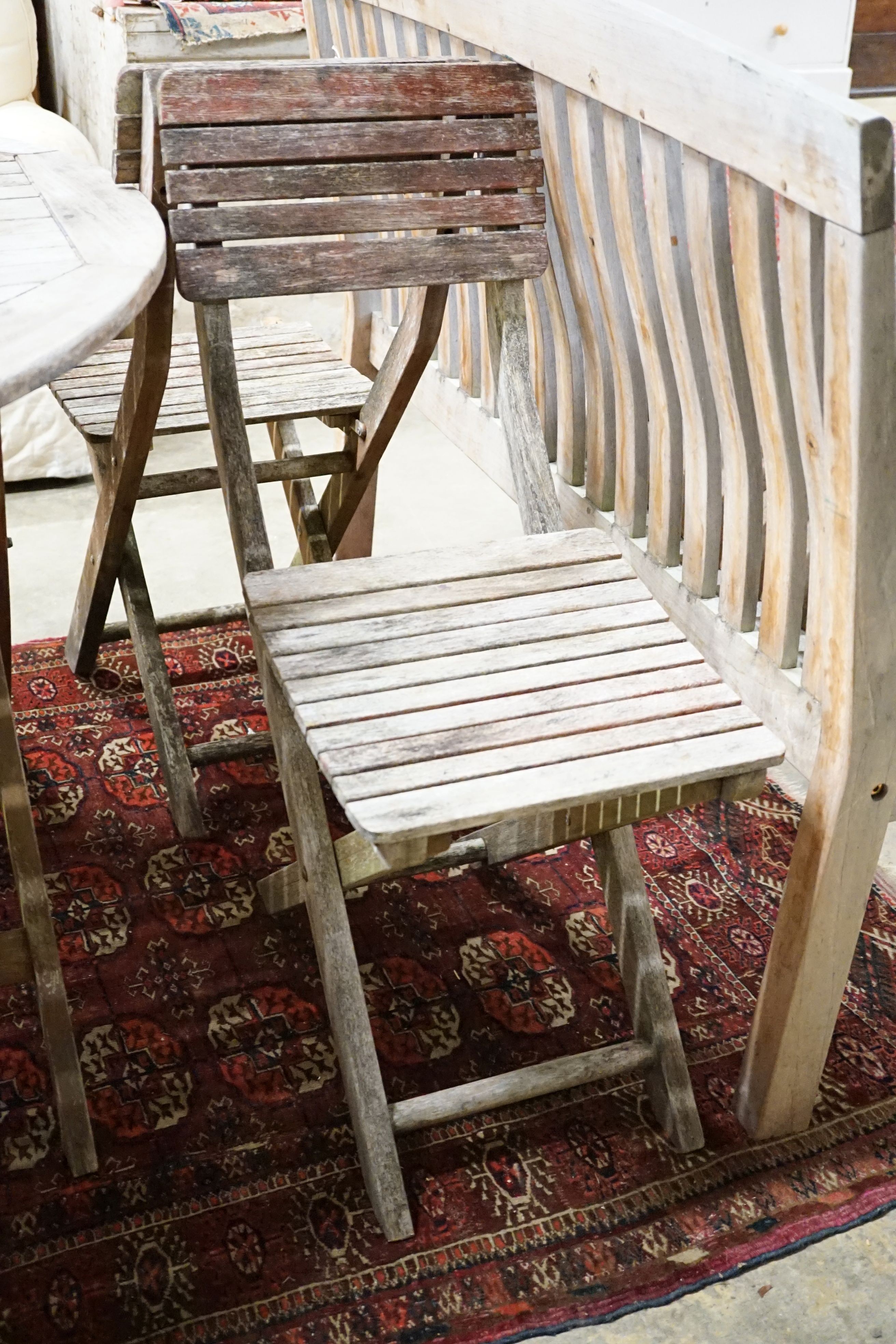 A weathered teak circular folding garden table and five folding chairs